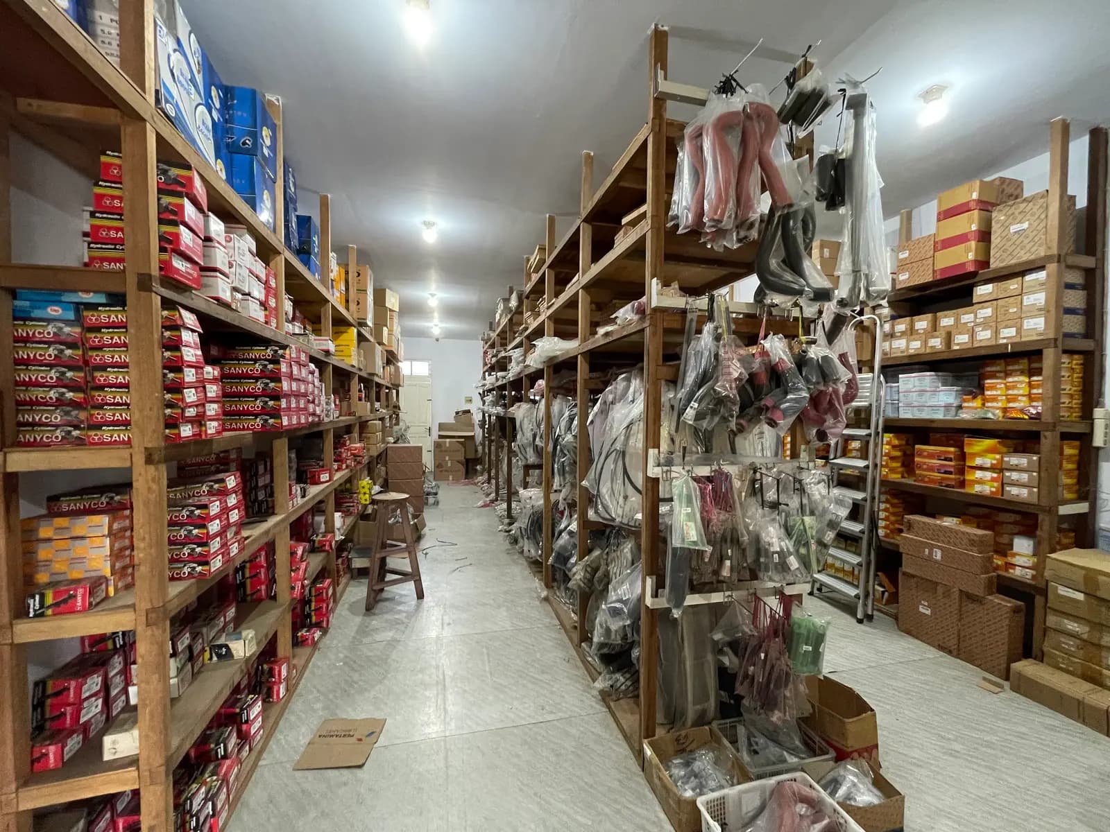 Lorong gudang dengan rak suku cadang dan selang